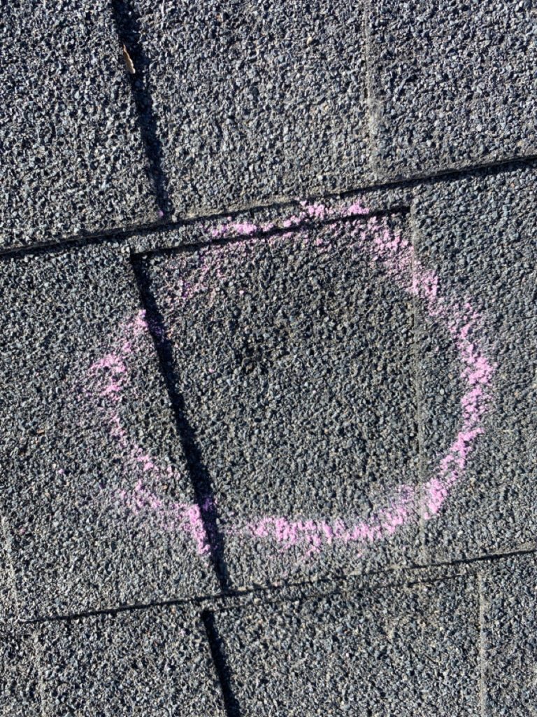 A circle drawn in pink chalk on the roof of a house.